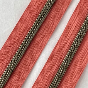 May include: Two strands of pink zipper tape with antique brass zipper teeth.