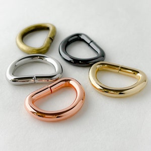 May include: Five metal D-rings in different finishes: gold, silver, copper, brass, and black. The rings are all the same size and shape.