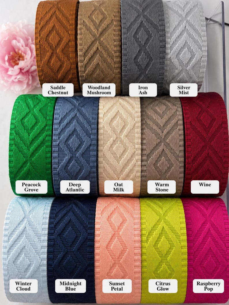 K&ouml;nnte beinhalten: Eine Sammlung von dreizehn Rollen gewebtem Band mit einem sich wiederholenden Rautenmuster. Die Farben sind beschriftet als Saddle Chestnut, Woodland Mushroom, Iron Ash, Silver Mist, Peacock Grove, Deep Atlantic, Oat Milk, Warm Stone, Wine, Winter Cloud, Midnight Blue, Sunset Petal, Citrus Glow und Raspberry Pop.