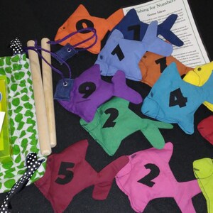 May include: A set of colorful felt fish with numbers 1 through 9, a bag with a set of addition flash cards, and two wooden fishing rods. The fish are designed for a game of fishing for numbers.