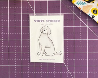 Op de afbeelding: Een witte vinyl sticker van een doodle hond die zit. De sticker is weerbestendig en heeft onderaan de tekst "Vinyl Sticker" en "sketchmoose.etsy.com".