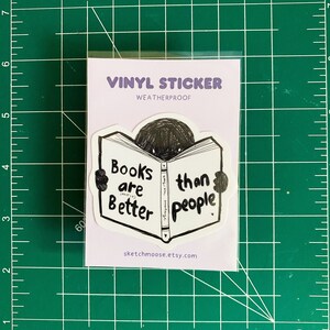 Könnte beinhalten: Ein weißer Vinyl-Aufkleber mit dem Text "Books are Better than people" in Schwarz. Der Aufkleber zeigt eine Cartoon-Figur, die ein Buch liest. Der Aufkleber trägt auch den Text "VINYL STICKER WEATHERPROOF" und die Website sketchmoose.etsy.com.
