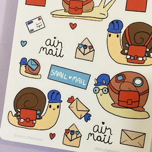 May include: A set of snail mail stickers featuring cute snails wearing blue hats and carrying red mailbags. The stickers also include envelopes, flowers, hearts, and the text "air mail" and "snail mail".