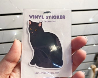 May include: A vinyl sticker featuring a black cat sitting with its tail curled around its legs. The sticker is weatherproof and has the text "VINYL STICKER WEATHERPROOF" and "sketchmoos.etsy.com" printed on it.