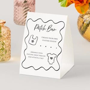 May include: A white ceramic mug with a black handle and the text "But First, Coffee" in a bold, black font. The mug is set against a blurred background, suggesting a cozy setting.