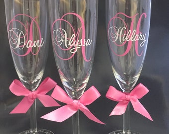 May include: Three champagne flutes with pink bows and personalized with the names Dani, Alyssa, and Hillary. The flutes are engraved with the text "Maid of Honor" and "Bridesmaid" and the date "March 2016".