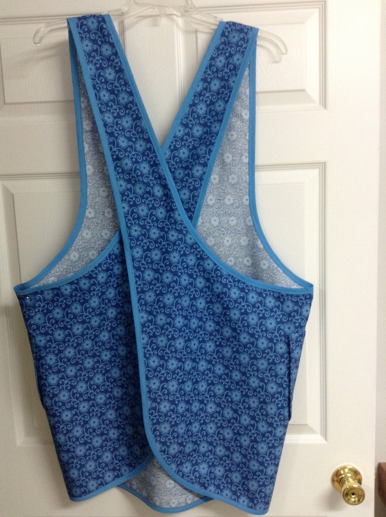 May include: A blue and white patterned apron with a criss-cross back design. The apron has a light blue trim.