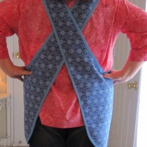 May include: A blue and white patterned apron with a criss-cross back design. The apron is worn over a red shirt.