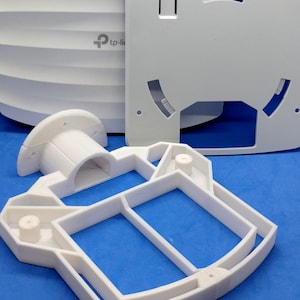 Może przedstawiać: Białe plastikowe części do routera TP-Link. Części obejmują kopułową osłonę, płaską płytę z okrągłym wycięciem i podstawę z prostokątnym otworem.