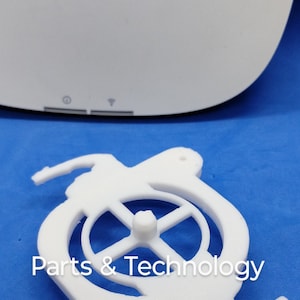 Può includere: Supporto di stampa 3D in plastica bianca con un'apertura circolare e un piccolo pomello al centro. Il supporto ha due bracci che si estendono sui lati. Il testo "Parts & Technology" è stampato sul supporto.