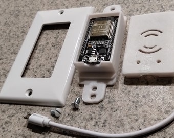Puede incluir: Una placa de pared blanca con un recorte rectangular, una carcasa blanca impresa en 3D con una placa de circuito dentro, una carcasa blanca impresa en 3D con un altavoz redondo, un cable USB blanco y dos tornillos.