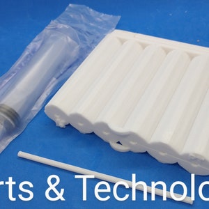 May include: A white plastic mold with multiple cylindrical cavities, a clear plastic syringe, and a white plastic stick. The mold is designed for creating candles or other crafts.