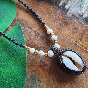 May include: A black cord necklace with white and gold beads and a shell pendant. The shell is wrapped in brown cord.