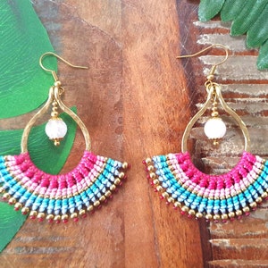May include: A pair of gold hoop earrings with a white bead and a colorful fringe of pink, blue, and gold beads.