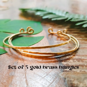 May include: Set of three gold brass bangles. The bangles are stacked on top of each other and have a hammered texture.
