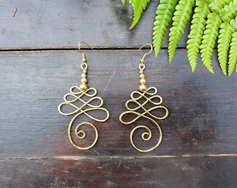 May include: A pair of gold-toned earrings with a spiral design and small round beads. The earrings are hanging from a wooden surface.