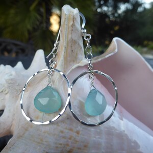 May include: Silver earrings with a hammered circle design and a light blue teardrop-shaped gemstone hanging from each circle.