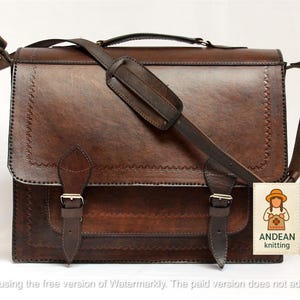 May include: A brown leather satchel with a shoulder strap and a top handle. The bag has two front buckles and decorative stitching around the edges. A tag with the text "ANDEAN knitting" is attached.