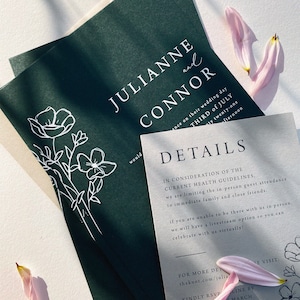 Op de afbeelding: Een groene en witte huwelijksuitnodiging met een bloemenontwerp. De uitnodiging kondigt het huwelijk van Julianne en Connor aan op de derde juli. De uitnodiging bevat details over het huwelijk en een website voor meer informatie.