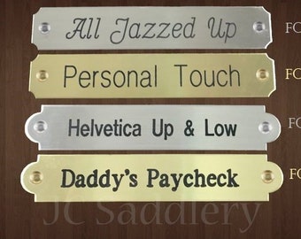May include: Four metal nameplates with engraved text. The plates are silver and gold, with text such as "All Jazzed Up" and "Daddy's Paycheck." Font numbers are listed next to each plate. The JC Saddlery logo is at the bottom.