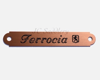 Peut inclure: Une étiquette métallique de couleur cuivre avec le mot "Ferrocia" en écriture cursive. L'étiquette a des extrémités arrondies avec des trous et un petit emblème à droite. Le texte "JC Saddlery" est au-dessus de l'étiquette.