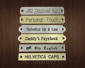 Peut inclure: Collection de plaques signalétiques métalliques gravées en argent et or. Les plaques présentent des phrases telles que "All Jazzed Up" et "Personal Touch". Une plaque présente une silhouette de cheval et l'inscription "Old English".