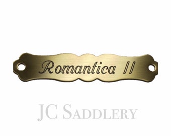 以下が含まれることがあります： 真鍮色の金属製ネームプレートで、優雅な筆記体で「Romantica II」と書かれています。 ネームプレートは装飾的なスカラップエッジと2つの取り付け穴があります。「JC Saddlery」の文字が下にあります。