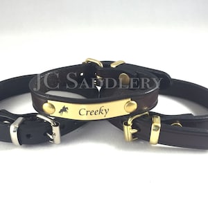 May include: Three leather horse tack pieces. The tack is brown and black with gold-colored hardware. One piece has a gold plate with the name "Creeky" and a horse silhouette. The logo "JC Saddlery" is in the bottom right.