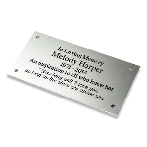 May include: A silver metal plaque with a memorial inscription for Melody Harper, 1971-2014. The inscription reads "In Loving Memory Melody Harper 1971-2014 An inspiration to all who knew her "How long will I love you as long as the stars are above you"