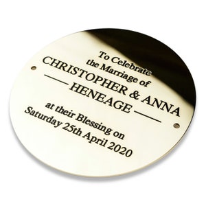 May include: A round, gold-coloured metal plaque with black engraved text that reads "To Celebrate the Marriage of Christopher & Anna Heneage at their Blessing on Saturday 25th April 2020".