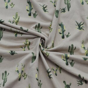May include: A beige fabric with a repeating pattern of green and yellow cacti. The fabric is folded and textured.