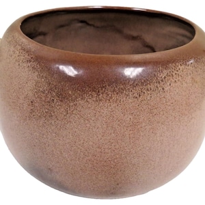 May include: A brown ceramic bowl with two small handles. The bowl has a rounded shape and a speckled texture. The rim and handles are a darker shade of brown, creating a gradient effect. The interior is a darker brown.
