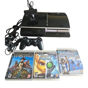 May include: A black PlayStation 3 console with a controller, camera, and three game cases. The game cases are for "Civilization Revolution", "Ratchet & Clank Future: A Crack in Time", and "Sports Champions".