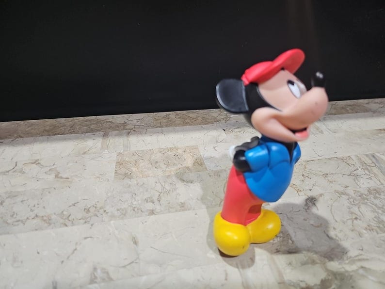May include: A red, blue, and yellow plastic toy figurine of Mickey Mouse wearing a red hat and a blue jacket.