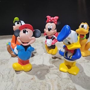 May include: A set of five colorful Disney character figurines, including Mickey Mouse, Minnie Mouse, Donald Duck, Goofy, and Pluto. The figurines are made of plastic and are in a playful, cartoon style.