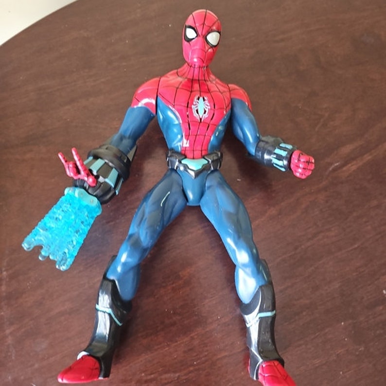 May include: A red and blue action figure of Spider-Man with a blue and white web shooter in his left hand. The figure has a black belt and a black and blue suit.