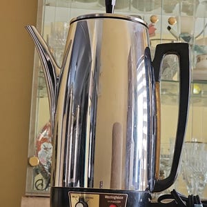 Könnte beinhalten: Edelstahl-Kaffeebereiter von Westinghouse mit schwarzem Sockel und Griff. Er hat einen Ausguss, einen Deckel mit schwarzem Knopf und ein Bedienfeld. Der Text "Stainless Steel" ist sichtbar.