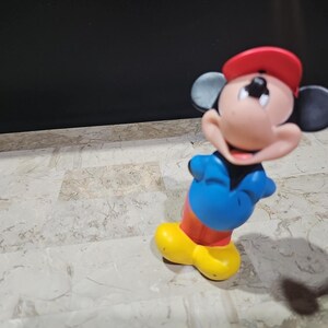 May include: A red, white, and blue Mickey Mouse figurine wearing a red baseball cap. The figurine is made of plastic and has a smiling face.