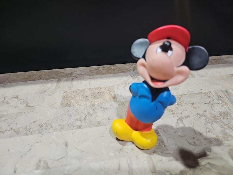 May include: A red, white, and blue Mickey Mouse figurine wearing a red baseball cap. The figurine is made of plastic and has a smiling face.
