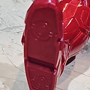 Pu&ograve; includere: Primo piano di un piede di action figure in plastica rossa con un design circolare sulla suola.