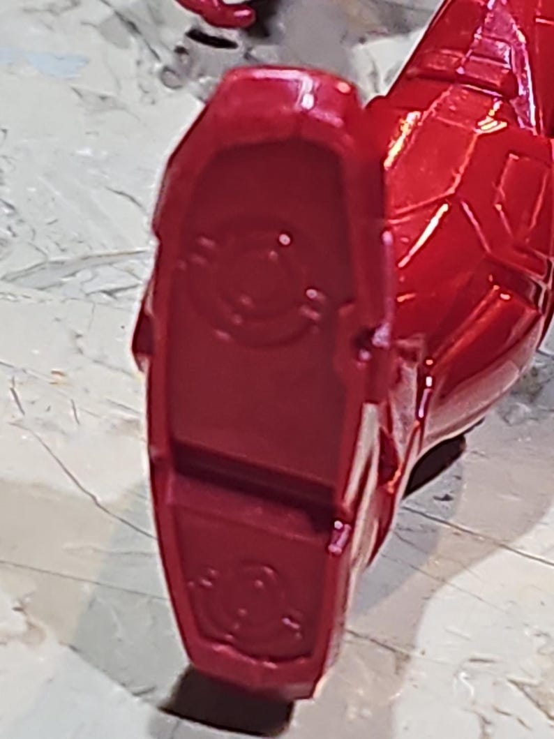 Pu&ograve; includere: Primo piano di un piede di action figure in plastica rossa con un design circolare sulla suola.
