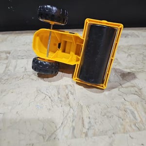 Puede incluir: Un veh&iacute;culo de construcci&oacute;n de juguete amarillo con ruedas negras y un rodillo negro. El veh&iacute;culo est&aacute; boca abajo.