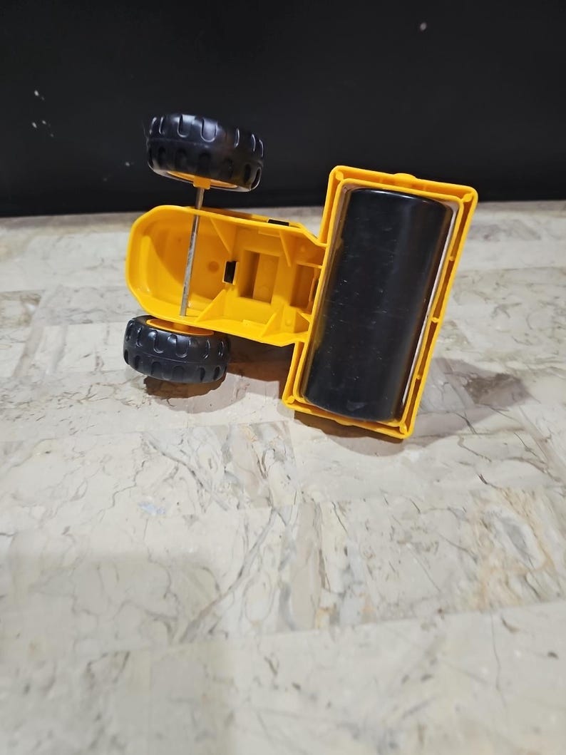 Puede incluir: Un veh&iacute;culo de construcci&oacute;n de juguete amarillo con ruedas negras y un rodillo negro. El veh&iacute;culo est&aacute; boca abajo.