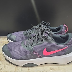 Pode incluir: Par de tênis roxos e pretos com sola branca e logotipo rosa da Nike. Os tênis têm cadarços cinza e detalhes rosa no calcanhar. Projetados para corrida e treino.