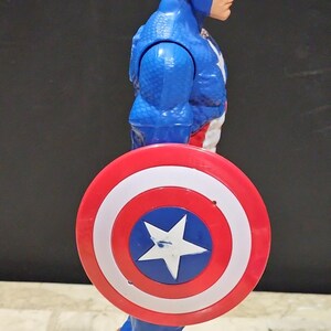May include: A blue and red plastic action figure of Captain America holding his red, white, and blue shield. The figure has a red, white, and blue costume with a star on the chest. The shield has a white star in the center.