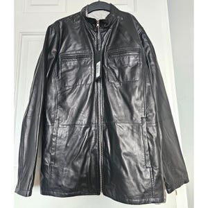 Peut inclure: Veste en cuir noir avec fermeture éclair, deux poches poitrine et deux poches basses. La veste a un col montant et une étiquette attachée à la fermeture éclair. La veste est suspendue à un cintre.