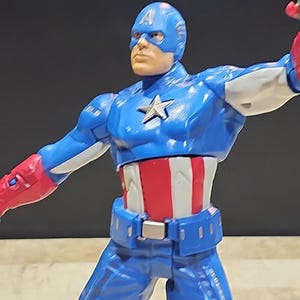 May include: A blue and red action figure of Captain America with a white star on his chest. The figure is posed with one arm outstretched and the other bent at the elbow.