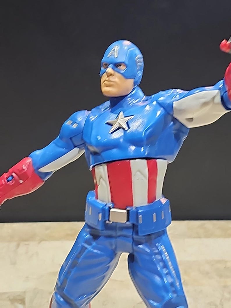 May include: A blue and red action figure of Captain America with a white star on his chest. The figure is posed with one arm outstretched and the other bent at the elbow.
