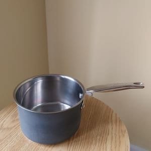 Könnte beinhalten: Ein Edelstahl-Topf mit einem silbernen Griff. Der Topf steht auf einer Holzoberfläche.