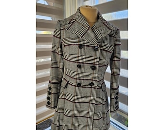 May include: A double-breasted plaid coat in black, white, and burgundy. The coat features a notched collar, black buttons, and a flared skirt. The sleeves have buttoned cuffs. The coat is displayed on a mannequin.